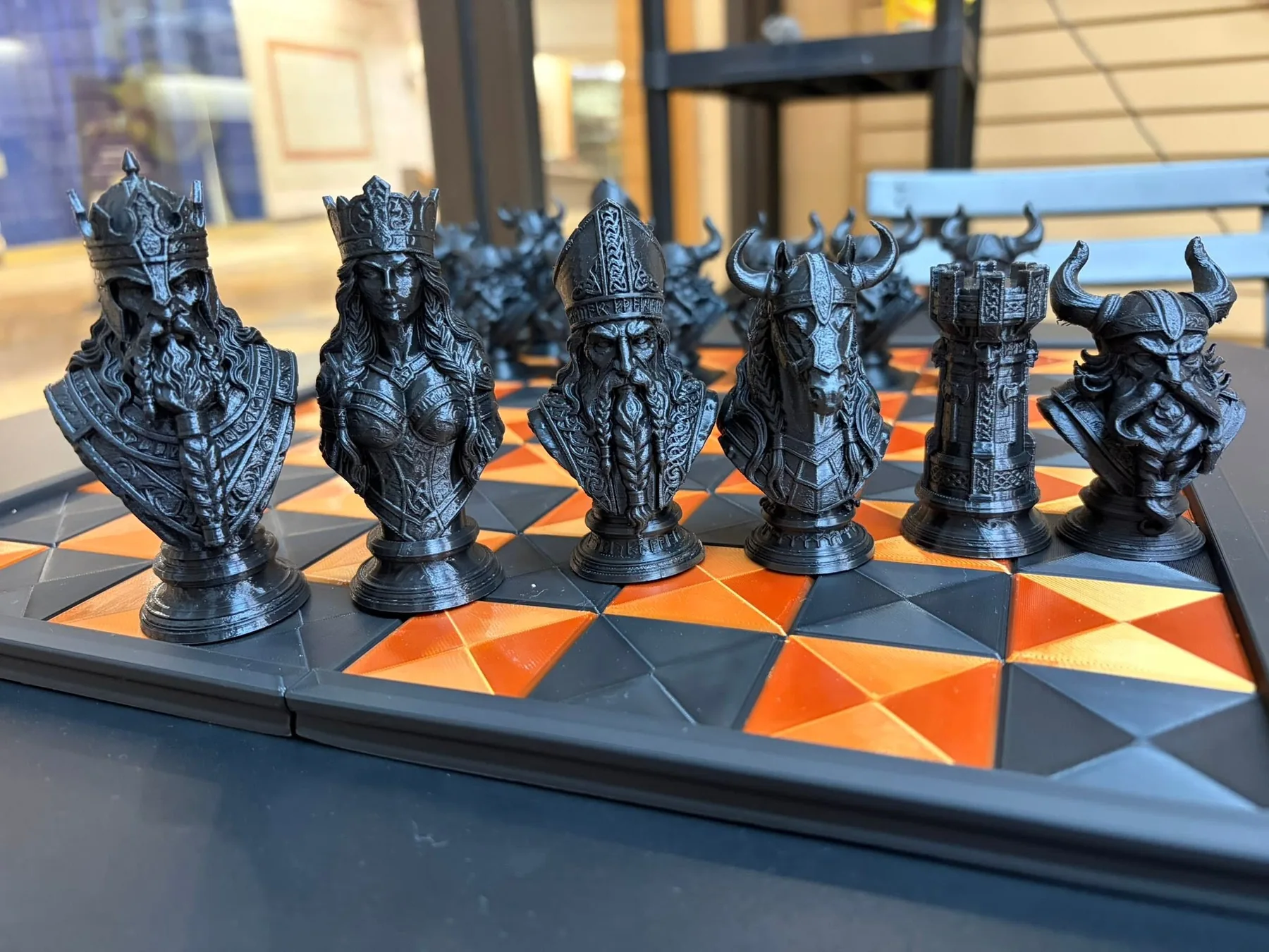 Detailed 3D-printed chess set with fantasy-style king, queen, bishop, knight, rook, and pawn pieces on an orange and black board.