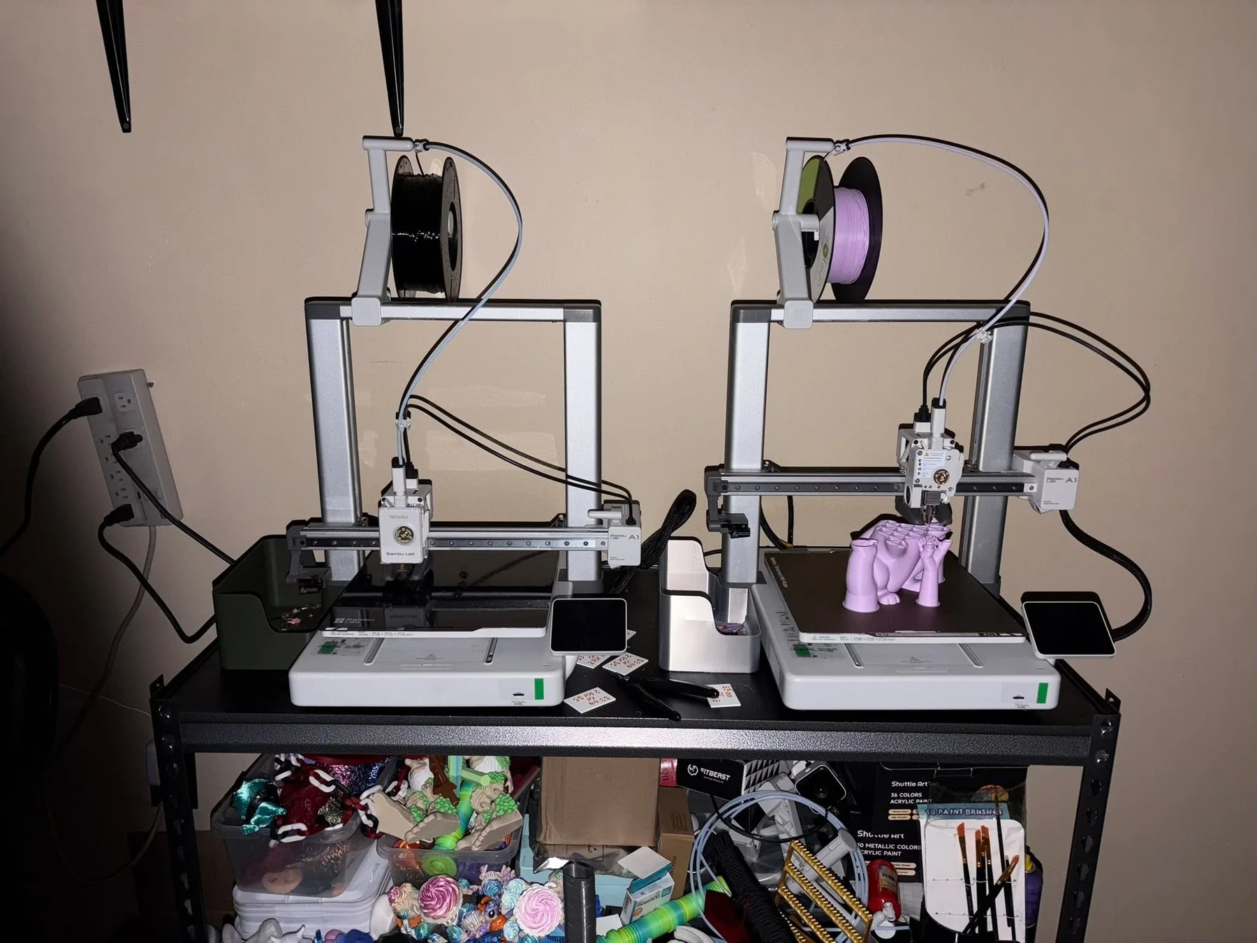 Two 3D printers set up side by side on a shelf, each mid-print.