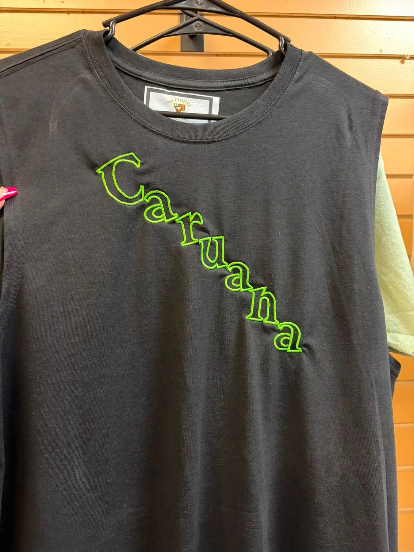 Black tank top with a name embroidered in green thread across the chest.