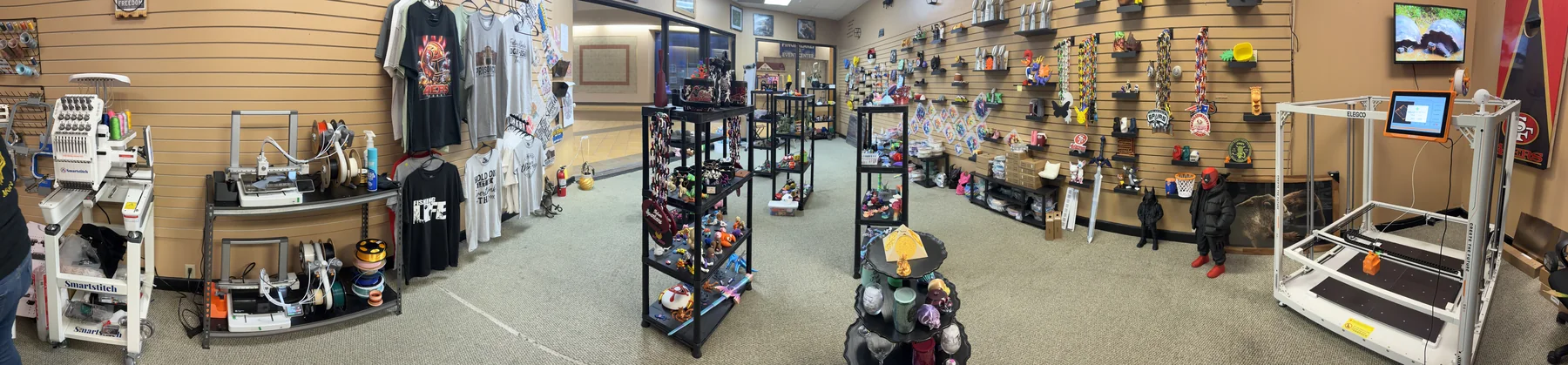 Panoramic view of the 3D Prints and More store interior, with apparel, 3D printers, and figure displays.